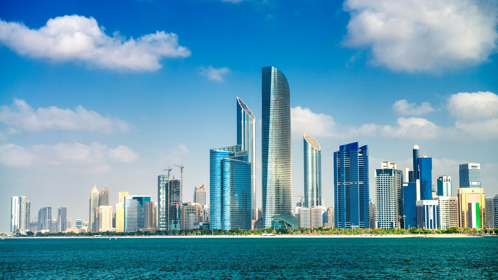 Abu Dhabi waterfront skyline across blue water in daylight.